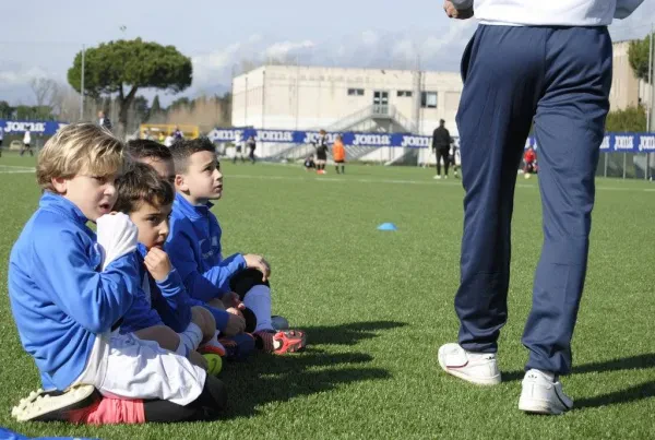 Young soccer players in blue listening attentively to coach on field